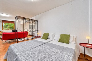 A hotel room with a bed, a red chair, a small table, and a window with a view of greenery.