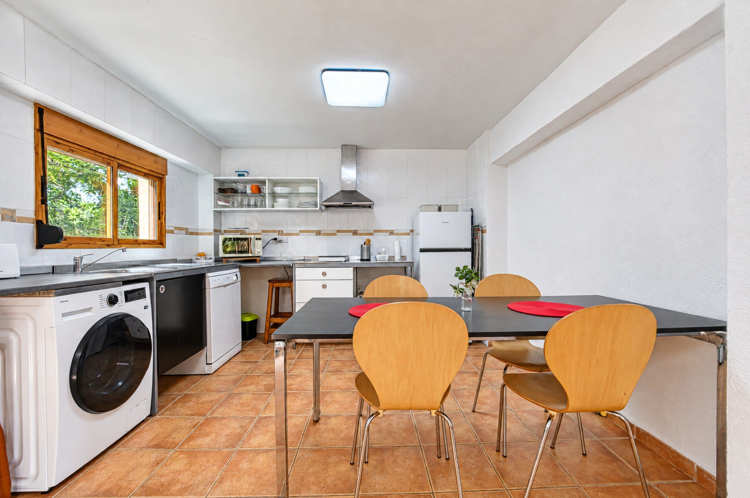 Cocina compacta con lavadora, una mesa de comedor con sillas y una ventana con vistas a zonas verdes.