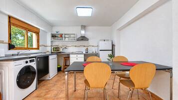 Cocina compacta con lavadora, una mesa de comedor con sillas y una ventana con vistas a zonas verdes.