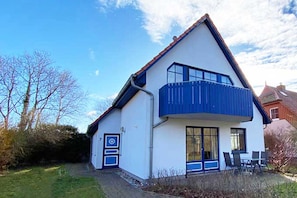 Ein zweistöckiges Haus mit Balkon, einer Tür mit blauem Rahmen und einer kleinen Sitzgelegenheit im Freien.