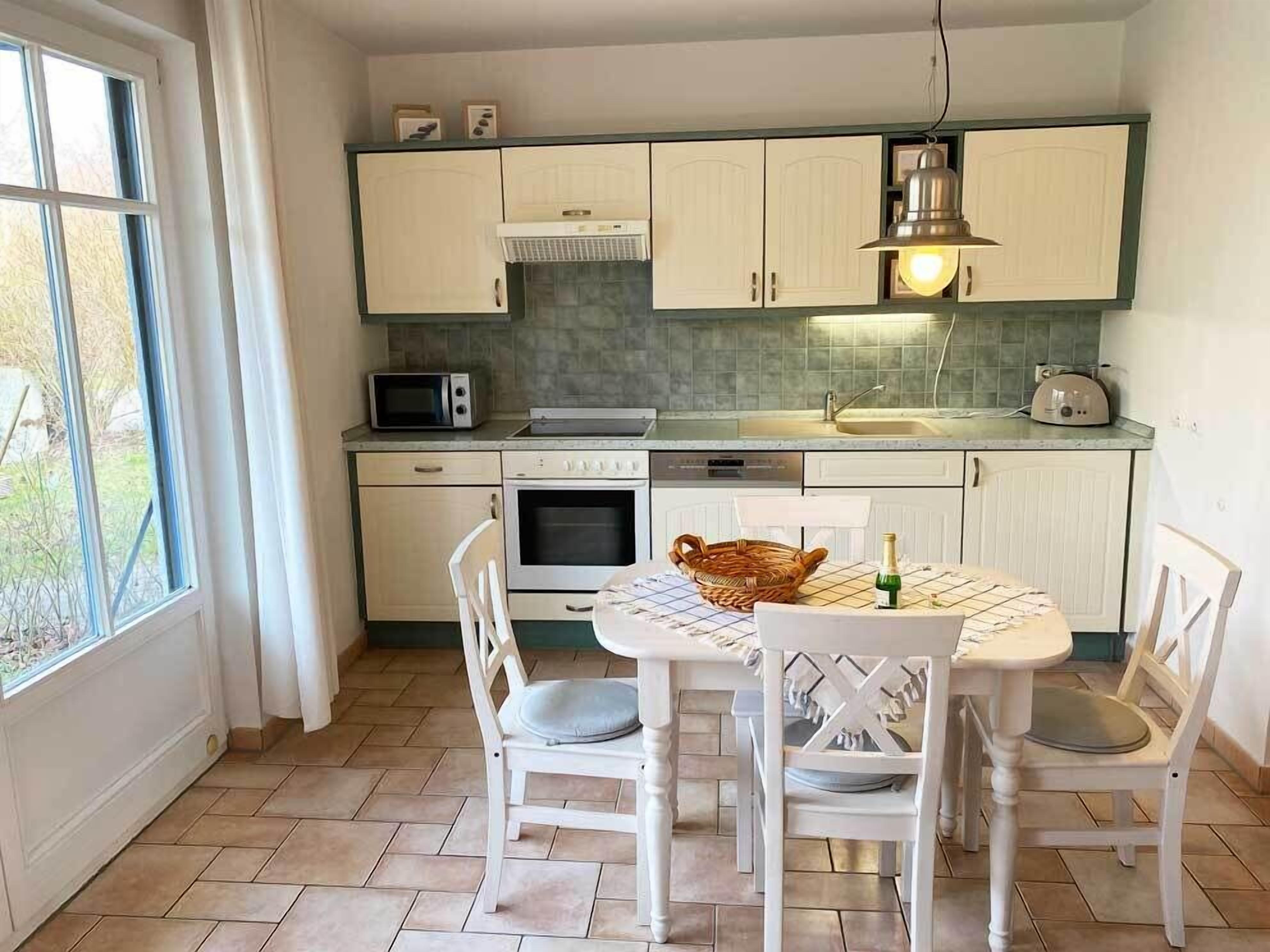A kitchen with white cabinets, a microwave, an oven, a sink, and a dining table with chairs.