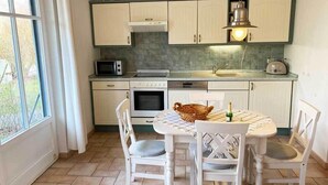 Une cuisine avec des meubles blancs, un four à micro-ondes, un four traditionnel, un évier et une table à manger avec des chaises.