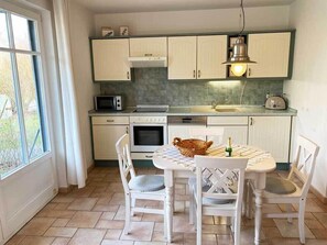 Eine Küche mit weißen Schränken, einer Mikrowelle, einem Backofen, einem Spülbecken und einem Esstisch mit Stühlen.