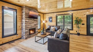 Ein Holzblockhaus-Interieur mit Kamin, Holzwänden, einer Couch und einem Fernseher.