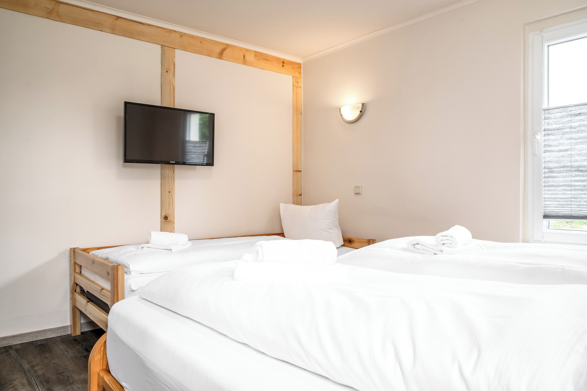 Habitació d'hotel amb dos llits, un televisor de pantalla plana muntat a la paret i una finestra amb persianes.