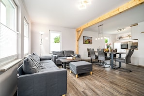 Ein modernes Wohnzimmer mit einer Couch, Hocker, Esstisch, Stühlen und einer Küchenzeile mit Geräten.