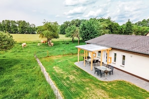 Ein Haus mit überdachter Terrasse, umzäunter Garten und Blick auf die umliegende Natur.