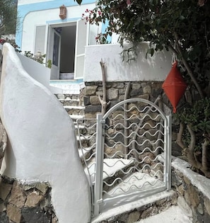A white building with a stone wall, a metal gate with a wavy pattern, and a red cone.