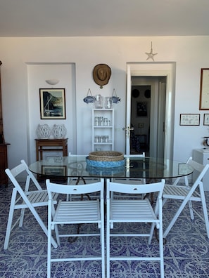 A dining area with a glass table, white chairs, a white cabinet, and patterned floor tiles.