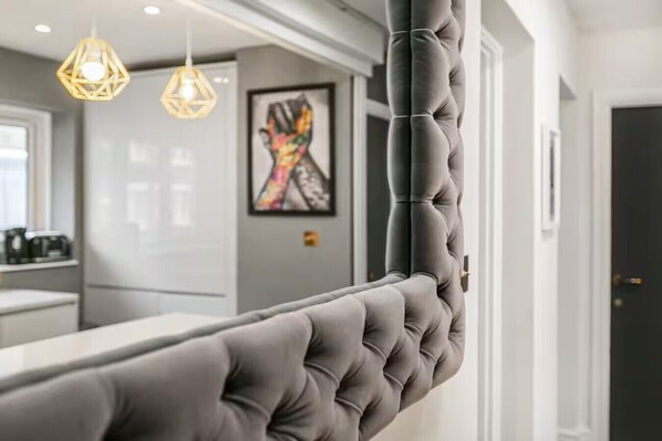 Ein graues, gestepptes Sofa in einer modernen Küche mit Pendelleuchten und einem farbenfrohen, abstrakten Gemälde an der Wand.