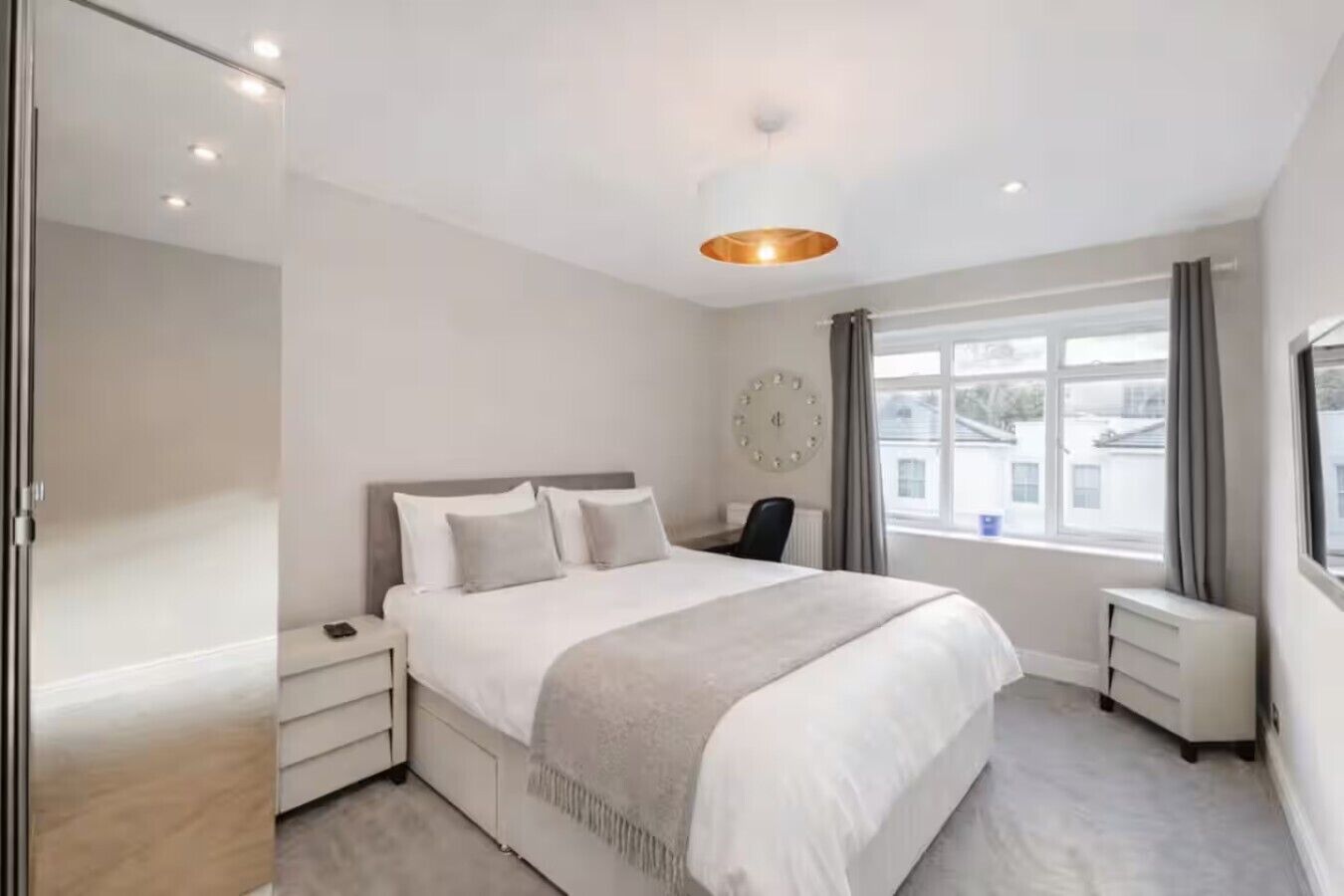 A modern bedroom with a large bed, bedside tables, a desk, and a window with curtains.
