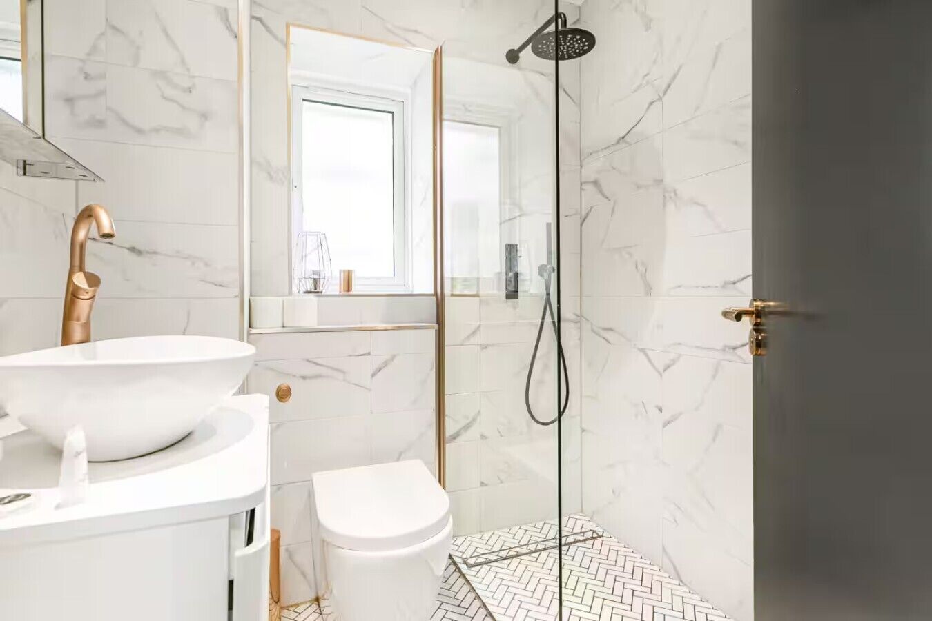 A modern bathroom with a white sink, gold faucet, and a glass-enclosed shower.