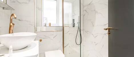 A modern bathroom with a white sink, gold faucet, and a glass-enclosed shower.