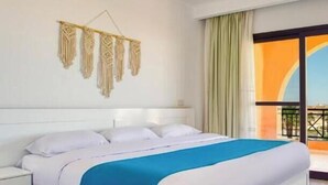 Ett hotellrum med en stor säng, ett vitt sängbord, en väggdekoration i makramé och utsikt över omgivningarna.