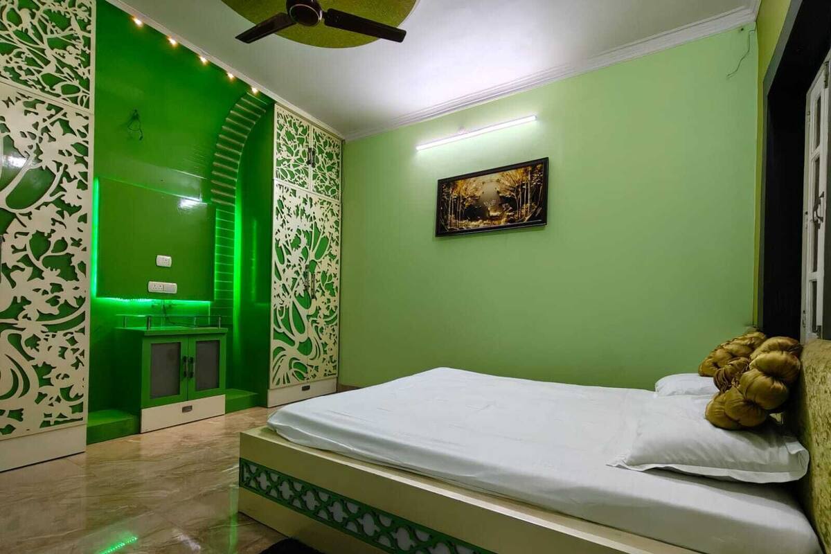 Un dormitorio con una cama, una pared verde, un cuadro y un ventilador de techo.