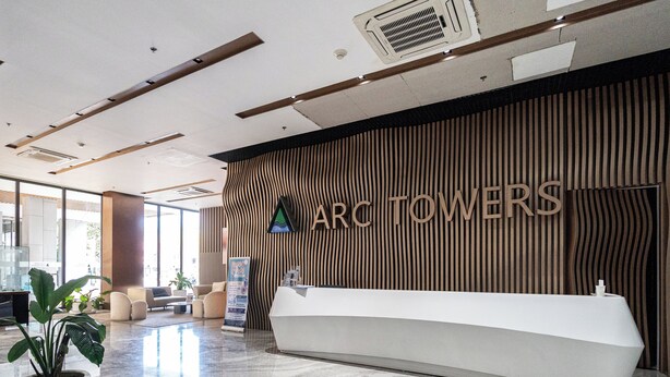 Un comptoir d’accueil au design moderne, un mur en bois aux lignes verticales et une enseigne indiquant « ARC TOWERS ».