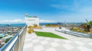 Une terrasse sur le toit avec un sol à carreaux, une petite pelouse et une vue sur un pont et le paysage urbain.