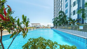 Une piscine entourée de verdure, avec un grand immeuble en arrière-plan.