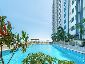Una piscina rodeada de vegetación y un edificio alto al fondo.