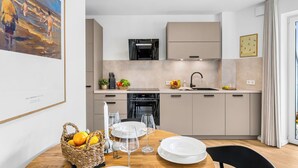 A modern kitchen with a dining area, featuring a Bosch refrigerator, a sink, and a dining table set with plates and glasses. - The View A04 Cloudsurfer  – Balcony, Garden Furniture, Shared Sauna, Parking (Dagebüll)