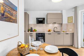 A modern kitchen with a dining area, featuring a Bosch refrigerator, a sink, and a dining table set with plates and glasses. - The View A04 Cloudsurfer  – Balcony, Garden Furniture, Shared Sauna, Parking (Dagebüll)