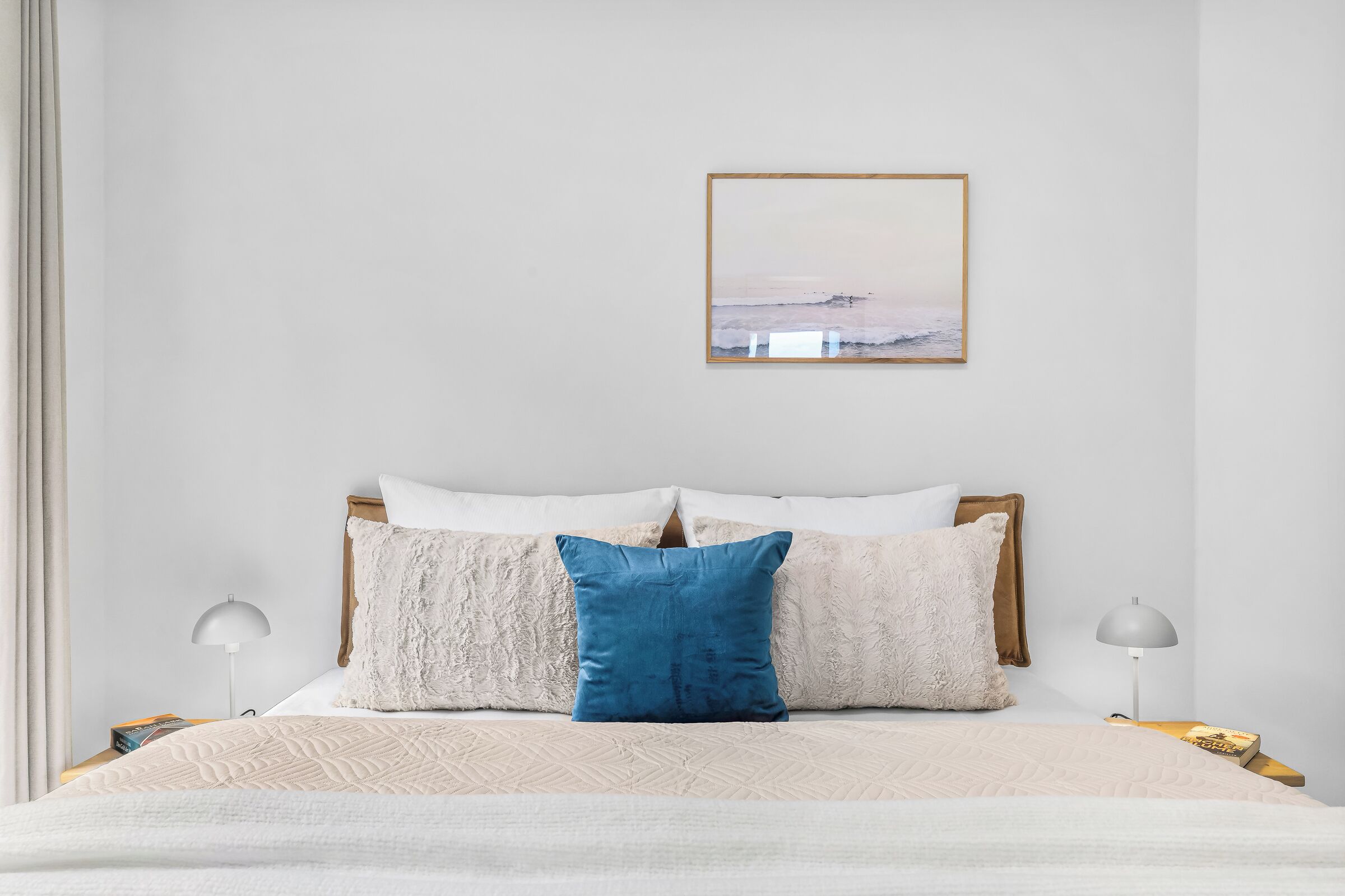 A bedroom with a bed, pillows, a framed picture on the wall, and bedside lamps.