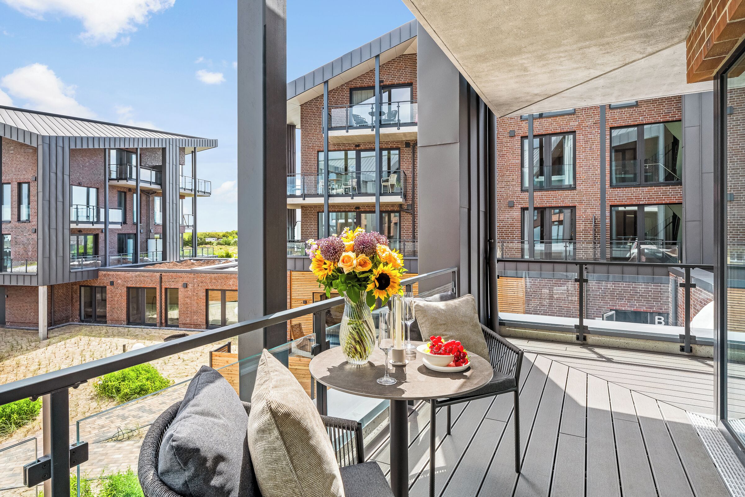 Un balcón con mesa lista para comer, un jarrón de flores y vistas a edificios modernos de ladrillo.