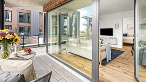 A modern apartment with a balcony, a dining area with a table and chairs, and a living room with a sofa and a TV. - The View A04 Cloudsurfer  – Balcony, Garden Furniture, Shared Sauna, Parking (Dagebüll)