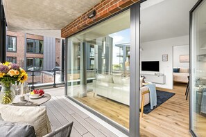 Eine moderne Wohnung mit Balkon, einem Essbereich mit Tisch und Stühlen sowie einem Wohnzimmer mit Sofa und Fernseher.