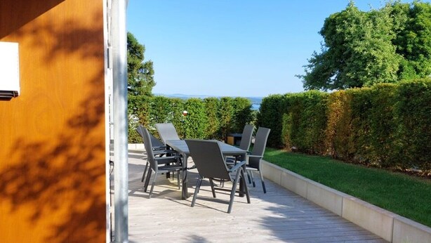 An outdoor patio with a table and chairs, a gravel pathway, and a view of the sea. - Time out by the lake: Luxurious vacation apartment with garden (Gaienhofen)