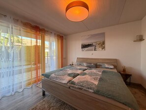 A bedroom with a bed, a nightstand, a wall-mounted lamp, a painting, and a sliding glass door leading to an outdoor area. - Time out by the lake: Luxurious vacation apartment with garden (Gaienhofen)