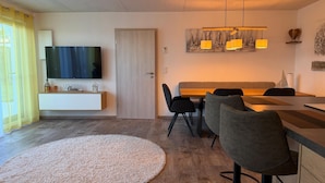 A modern living room with a flat-screen TV, a dining area with a wooden table and chairs, and a large round rug on the floor. - Time out by the lake: Luxurious vacation apartment with garden (Gaienhofen)