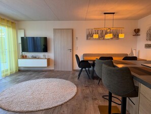 A modern living room with a flat-screen TV, a dining area with a wooden table and chairs, and a large round rug on the floor. - Time out by the lake: Luxurious vacation apartment with garden (Gaienhofen)
