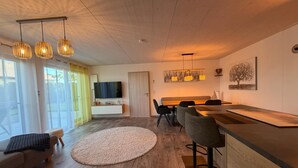 A modern living room with a flat-screen TV, wooden flooring, a round rug, and a dining area with a wooden table and chairs. - Time out by the lake: Luxurious vacation apartment with garden (Gaienhofen)