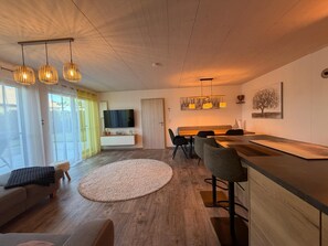 A modern living room with a flat-screen TV, wooden flooring, a round rug, and a dining area with a wooden table and chairs. - Time out by the lake: Luxurious vacation apartment with garden (Gaienhofen)