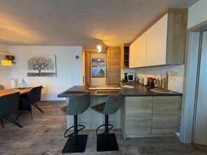 A modern kitchen with a central island, bar stools, and a dining area with a table and chairs. - Time out by the lake: Luxurious vacation apartment with garden (Gaienhofen)