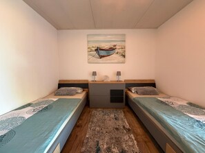 A room with two single beds, a small table with lamps, a painting on the wall, and a rug on the floor. - Time out by the lake: Luxurious vacation apartment with garden (Gaienhofen)