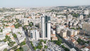 Vista aérea de un paisaje urbano con un moderno rascacielos destacado en el centro, rodeado de edificios residenciales y comerciales.