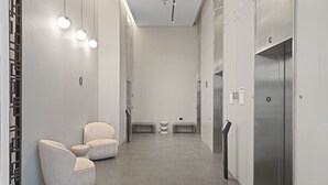Un ascensor moderno con detalles metálicos, un área de espera con dos sillones acolchados y un diseño limpio y minimalista.