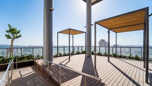 Terraza en la azotea con suelo de madera, barandillas metálicas y pérgolas de madera abiertas.