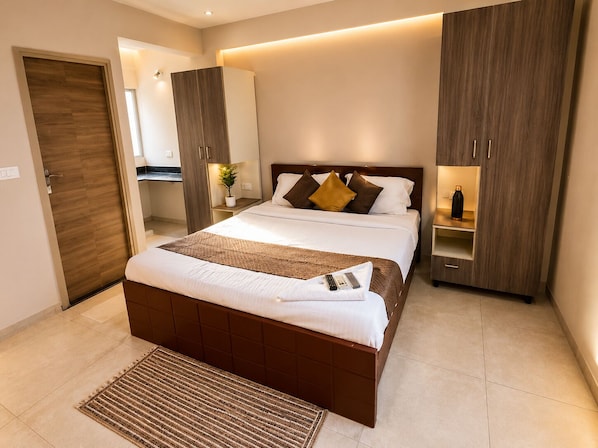 A modern bedroom with a large bed, a bedside table, a wardrobe, and a mirror.