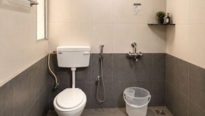 A bathroom with a toilet, shower, and a small shelf with toiletries.