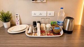 A hotel room with a tray of breakfast items, a kettle, a water bottle, a plant, a digital clock, and a power outlet.
