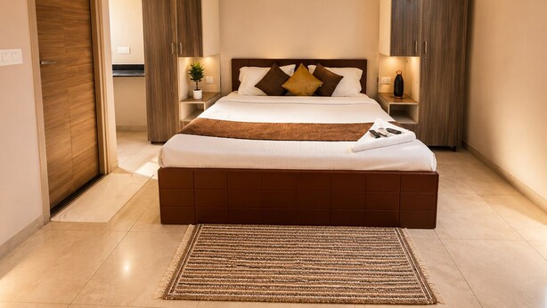 A modern bedroom with a large bed, bedside tables, a nightstand, a wall-mounted lamp, and a door.