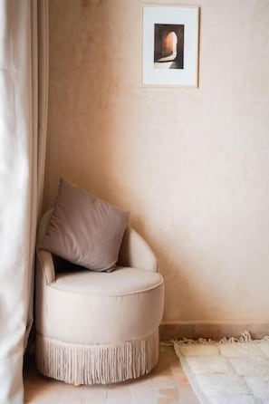 Quarto de canto com uma cadeira redonda, um quadro na parede e um tapete texturizado no chão.