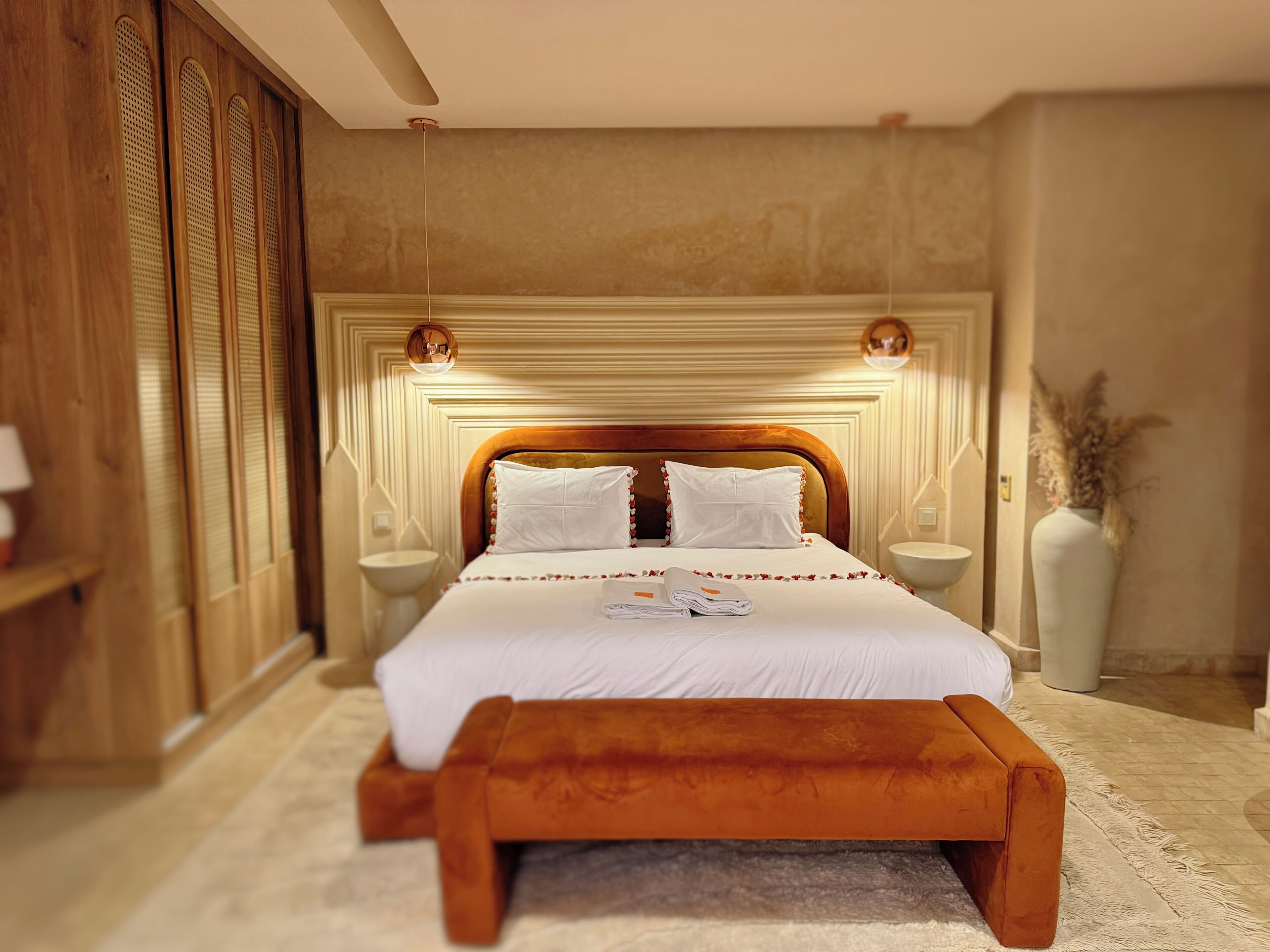 A hotel room with a large bed, bedside tables, a wooden headboard, and a decorative vase.