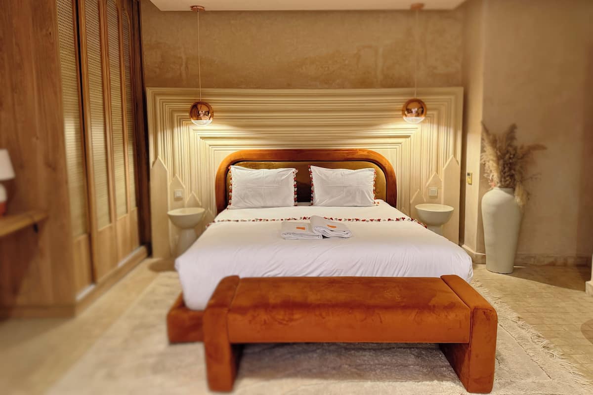 Une chambre d’hôtel avec un grand lit, des tables de chevet, une tête de lit en bois et un vase décoratif.