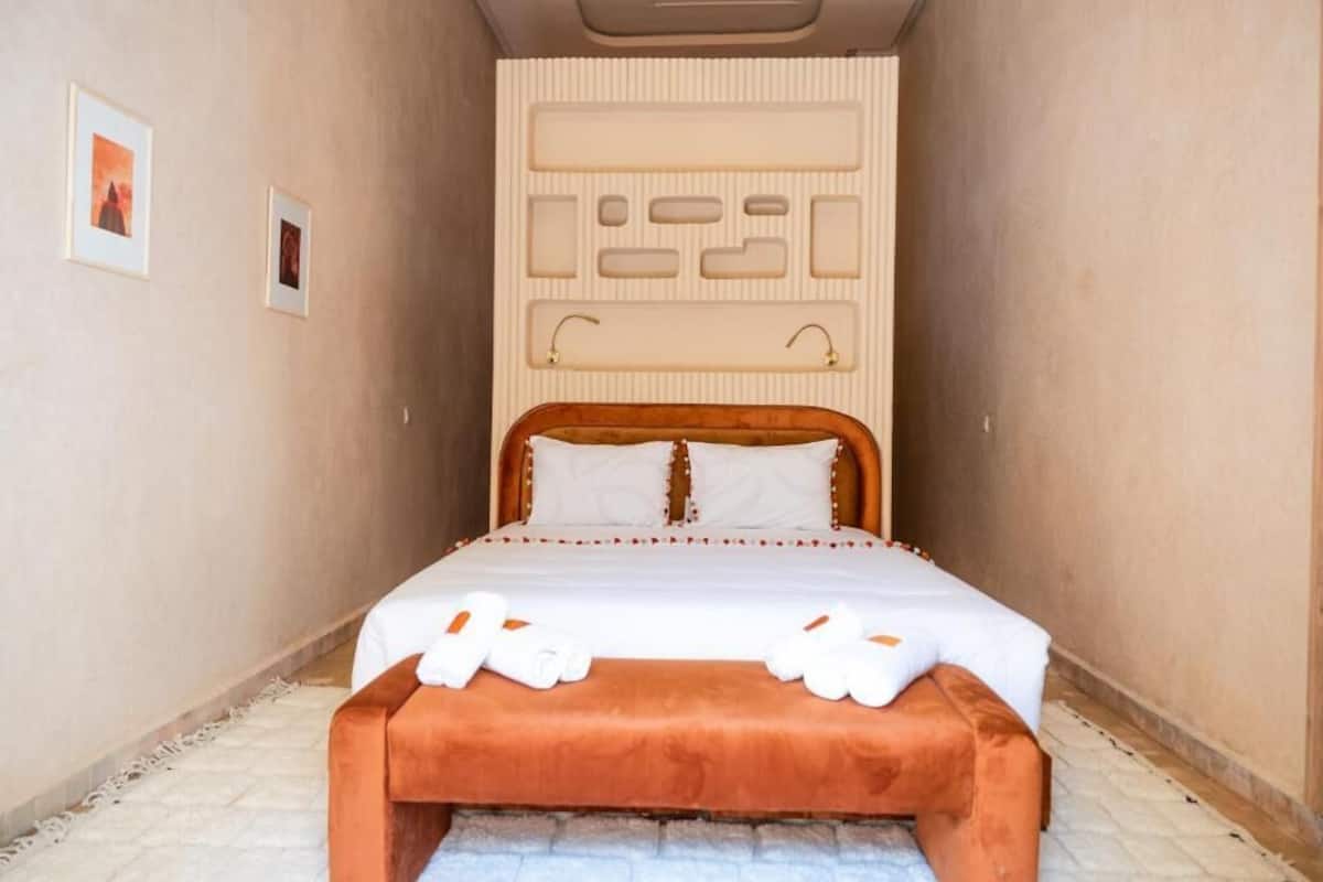 Une chambre d’hôtel étroite, comprenant un lit, une banquette et un meuble de rangement fixé au mur.