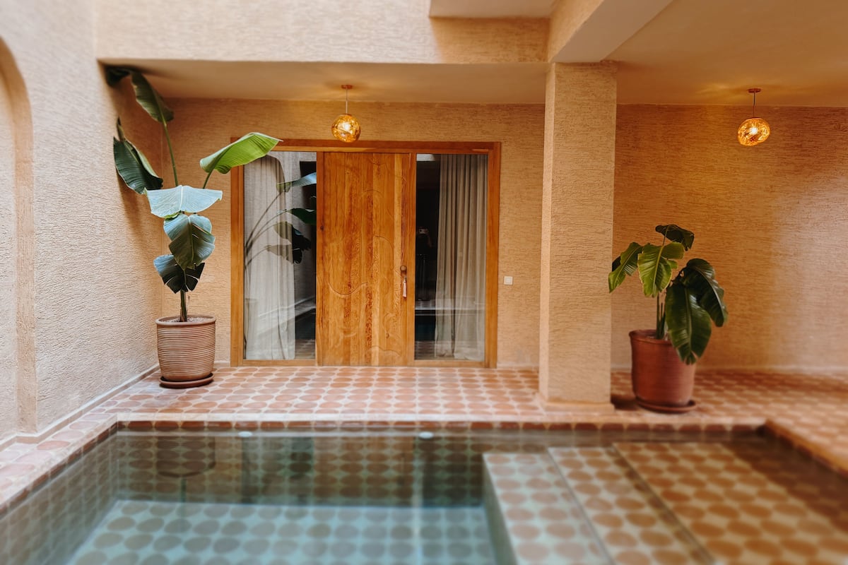 Un espace piscine doté d’un sol carrelé, d’une porte en bois et de plantes en pot.