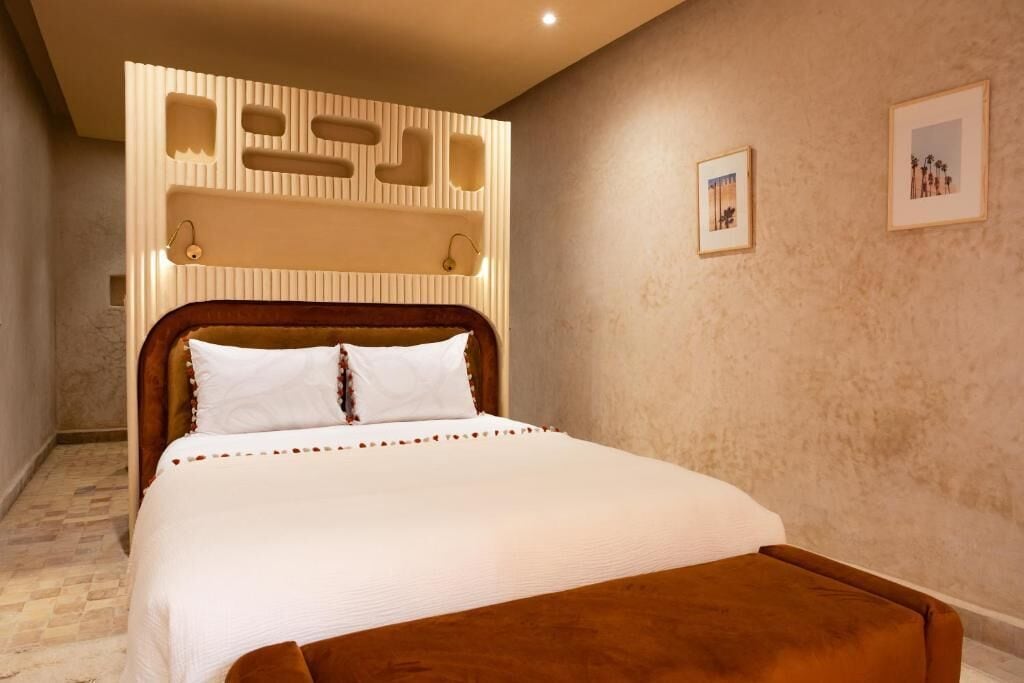 Un dormitorio con cama, cabecera de madera, reposapiés marrón y pared texturizada con iluminación empotrada.
